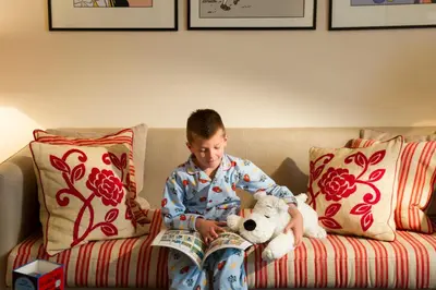 a boy sitting on a couch reading a book with a teddy bear at Hotel Amigo, a Rocco Forte Hotel in Brussels
