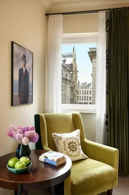 a living room with a chair and a table and a window at Hotel Amigo, a Rocco Forte Hotel in Brussels