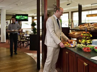 a man in a suit standing at a counter with a plate of food at ibis Hotel Brussels Expo Atomium in Brussels