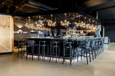 a bar with black bar stools and chandeliers at nhow Brussels Bloom in Brussels