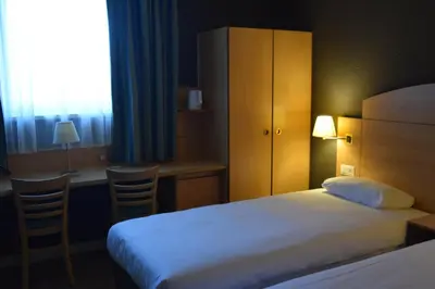 a hotel room with a bed and a desk and a window at DC Sleep & Go Brussels West in Brussels
