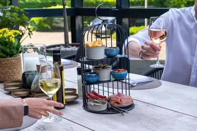 a person holding a glass of wine next to a plate of food at Van der Valk Hotel Antwerpen in Antwerp