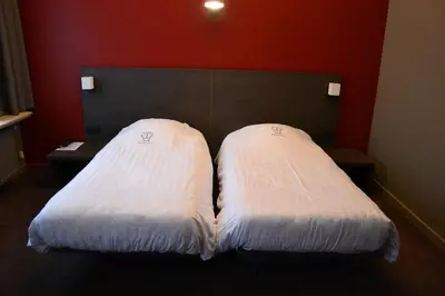 two white beds in a room with a red wall at Hotel De Franse Kroon in Diest