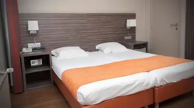 a bedroom with a large bed with an orange blanket at Hotel Castel in Ghent