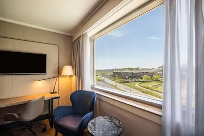 a hotel room with a desk and a large window at NH Brussels Airport in Diegem