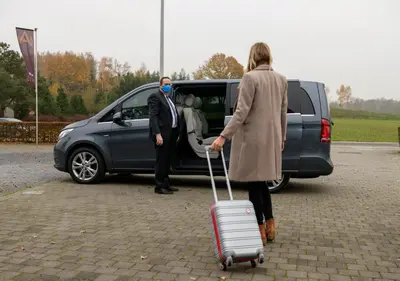 a woman pulling a suitcase in front of a van at Axis Hotel in Kortenberg