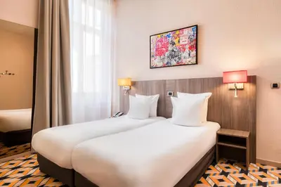 two beds in a hotel room with two lamps at ALMA Grand Place Hotel in Brussels