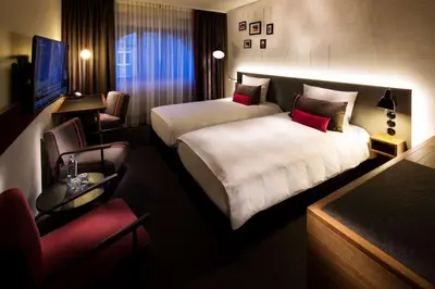 a hotel room with two beds and a chair at pentahotel Leuven in Leuven