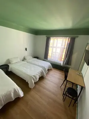 a bedroom with two beds and a table and two windows at Hotel Windsor in Brussels