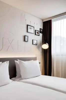 a bedroom with a bed with white sheets and pictures on the wall at Pentahotel Brussels Airport in Diegem
