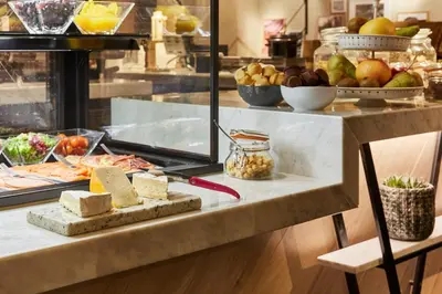 a buffet with cheese and other food on a counter at Hotel Indigo Antwerp City Centre by IHG in Antwerp