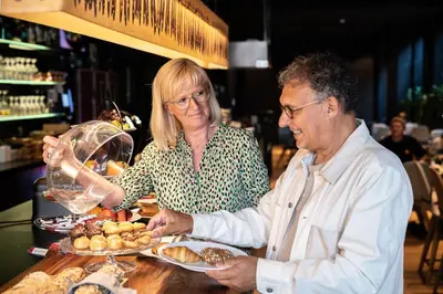 a man and a woman standing at a table with food at Hotel Vé in Mechelen