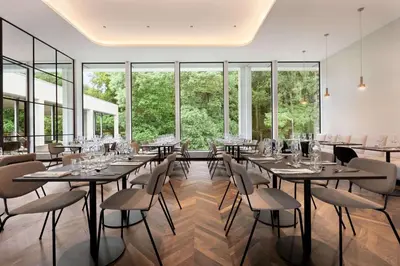a dining room with tables and chairs and large windows at Hotel Dolce La Hulpe Brussels in La Hulpe