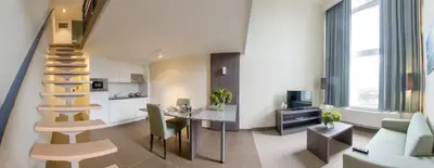 a living room with a staircase and a table and chairs at Arass Hôtel & Business Flats in Antwerp