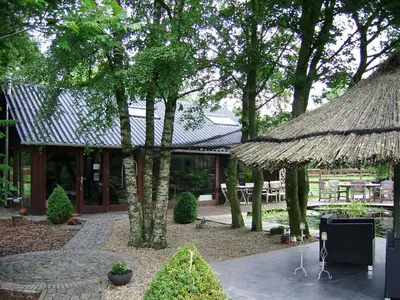 a building with a straw roof and a patio at Het Schalks Genot in Poppel