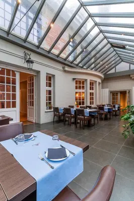 a dining room with tables and chairs and a glass ceiling at Hotel Villa Monte in Heist-op-den-Berg