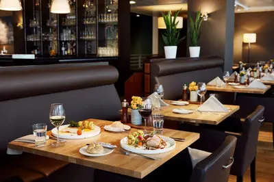 a restaurant with wooden tables with food and wine glasses at Lindner Hotel Antwerp, part of JdV by Hyatt in Antwerp