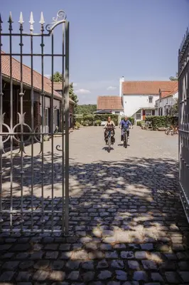 two people riding bikes down a street behind a gate at B&B Hullebrug in Heist-op-den-Berg