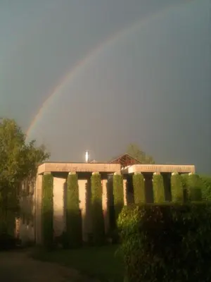 a rainbow in the sky over a building with bushes at Le Jardin Des Sources in La Hulpe