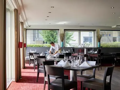 a man standing in a dining room with tables and chairs at Gosset Hotel in Groot-Bijgaarden