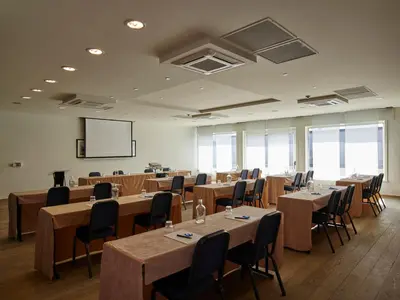 a conference room with tables and chairs and a screen at Gosset Hotel in Groot-Bijgaarden