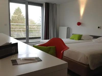 a hotel room with two beds and a red chair at Hotel Corbie Geel in Geel