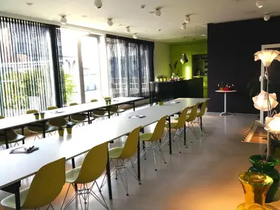 a row of tables and chairs in a room with windows at Hotel Corbie Geel in Geel
