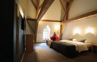 a woman sitting on a red suitcase in a room with a bed at Hotel The Lodge Heverlee in Leuven
