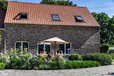 a group of people sitting under an umbrella in front of a brick building at B&B 't Heirweggoed in Assenede