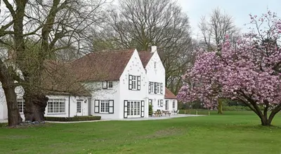 a white house with a flowering tree in the yard at B&B Domein Rodin in Oud-Turnhout