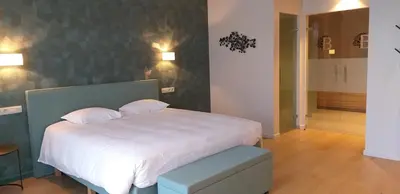 a bedroom with a large white bed with a blue stool at Hotel B - Boskapelhoeve in Buggenhout