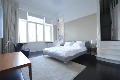 a white bedroom with a bed and a desk and window at Appartement Chic in Brussels