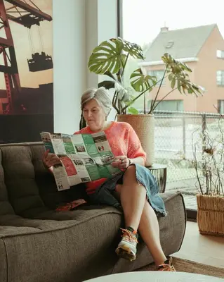 a woman sitting on a couch reading a newspaper at TRUST Hotel in Beveren