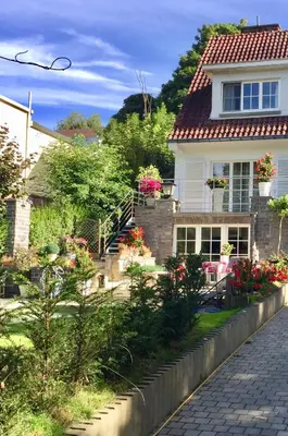 a white house with flowers in the front yard at Studio swimming pool BXL in Dilbeek