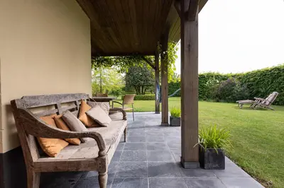a porch with a wooden bench on a patio at Chez Maintje in Bassevelde