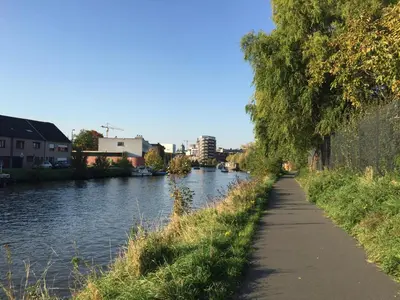 a path next to a river with trees and buildings at Scheldepunt in Ghent