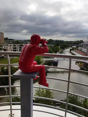 a person in a red suit sitting on a ledge at Scheldepunt in Ghent