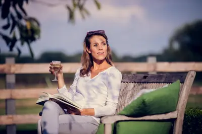 a woman sitting on a bench reading a book and holding a drink at De Schaapskooi in Kasterlee