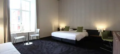 a bedroom with a bed and two chairs and a window at Hotel The Lodge Vilvoorde in Vilvoorde