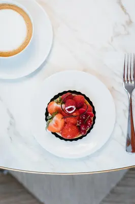a fruit tart on a plate on a table with a cup of coffee at Pillows Grand Boutique Hotel Reylof Ghent in Ghent