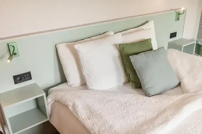 a bed with white and green pillows on it at Abalona Hotel & Apartments in Dendermonde