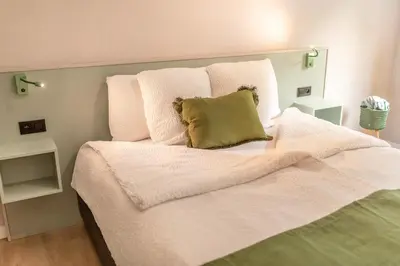 a white bed with a green pillow on it at Abalona Hotel & Apartments in Dendermonde
