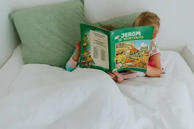a little girl laying in bed reading a book at Hotel Jerom in Kalmthout