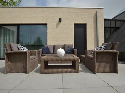 a patio with two wicker chairs and a table at Lovely holiday home 'Walleken' with a pond in Eekhout