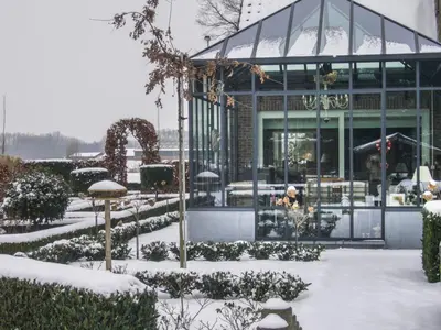 a building covered in snow in front of a garden at De Moeraseik in Zele