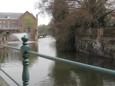 a river with a green railing next to a bridge at Lovely Guesthouse Lier in Lint