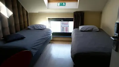 two beds in a small room with a window at Leuven City Hostel in Leuven