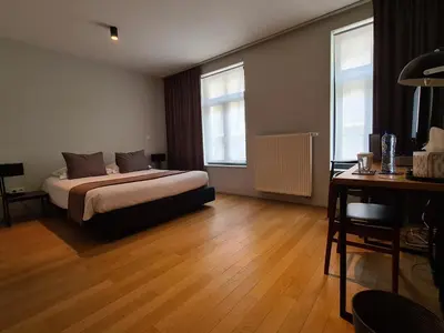 a bedroom with a bed and a desk and two windows at B&B A Côté du Cinquantenaire in Brussels