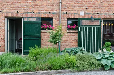 a brick building with green doors and flowers in a garden at B&B Euverbraeke in Beveren