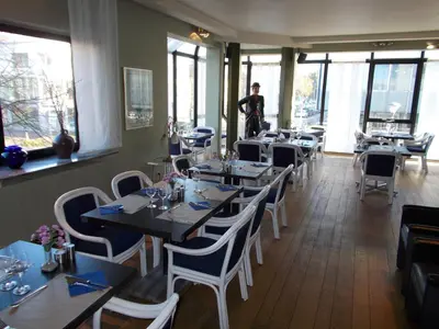 a restaurant with tables and chairs and a man standing in the background at Hotel De Swaen in Herentals
